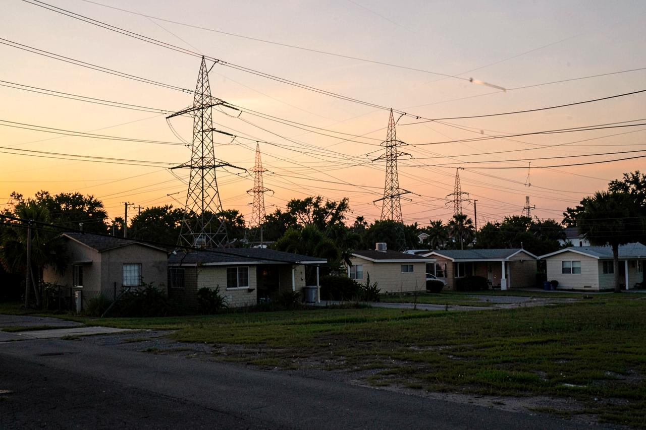 High-voltage transmission towers and power lines behind a row of Florida homes at dusk